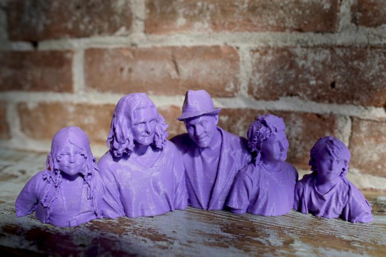 In this Aug. 14, 2014 photo, a plastic bust statue of Kevin Micelli, center, and his family, made by a 3-D scanner and printer, sits on a shelf inside Micelli's coffee shop in New York. Micelli purchased the 3-D scanning and printing services at the Cubo toy store next door to his shop. With the old studio portrait supplanted by the selfie, 3-D scanning services provide a new reason for people to go to a store and stand stock-still in front of a camera. (AP Photo/Julie Jacobson)