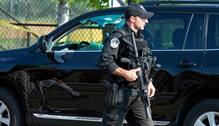 A Capitol Hill Police officer walks past an automobile with the driver's window damaged at the scene of a shooting in Alexandria, Va., Wednesday, June 14, 2017, where House Majority Whip Steve Scalise of La. was shot at a Congressional baseball practice. (AP Photo/Cliff Owen)