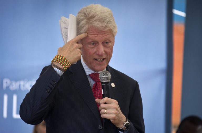 Former President Bill Clinton gestures while wearing a bracelet given to him by the pupils, as he and Chelsea Clinton talk about their foundation's 