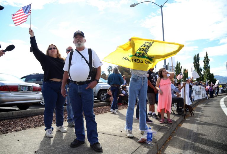 Demonstrators watch as President Obama arrives at Roseburg Regional Airport in Roseburg, Ore., Friday, Oct. 9, 2015. (AP Photo/Ryan Kang)