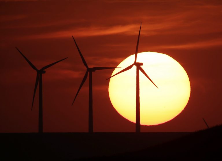 In this Aug. 23, 2013 file photo wind turbines are silhouetted by the setting sun as they produce electricity near Beaumont, Kan. The plains of Kansas could be a treasure trove in the nation's growing effort to harness clean energy. But a major proposal to move wind-generated electricity from Kansas to the East is running into a roadblock: Farmers who don't want high-power transmission lines on their land. (AP Photo/Charlie Riedel, File)