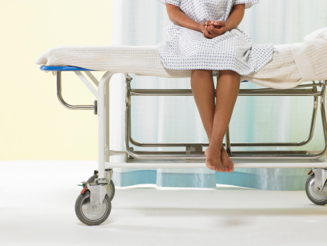 Female patient sitting on gurney in hospital gown, low section