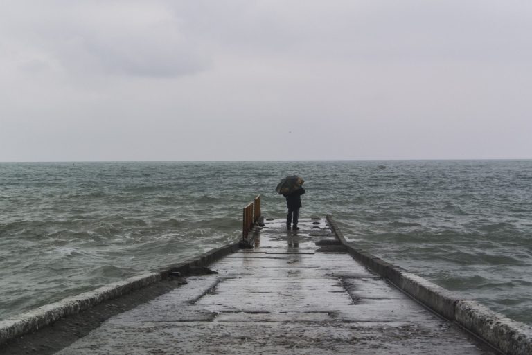 In this photo taken Thursday, Jan. 23, 2014, a man with an umbrella stands on the pier in central Sochi, Russia.  The Russian Black Sea resort of Sochi is hosting the Winter Games on Feb. 7-23.  (AP Photo/Nataliya Vasilyeva)