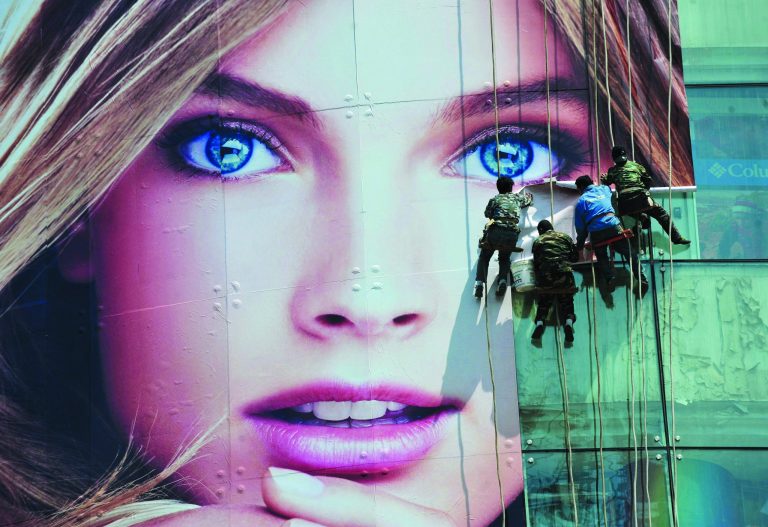 In this photo taken on Thursday, May 3, 2012, workers paste a giant advertisement poster for foreign product on the window of a department store in Shenyang in northeast China's Liaoning province. China's government has taken the unusual step of publicly denying it passed the United States last year as the world's biggest trader - a politically sensitive status. (AP Photo) CHINA OUT