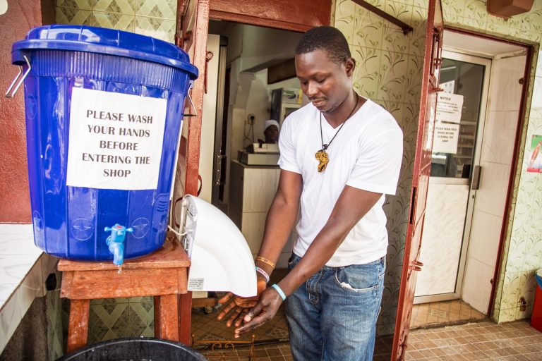 In this photo taken on Sunday, Sept. 14, 2014, a man dries his hands after washing them with chlorine outside a shop in the city of  Freetown, Sierra Leone.  Shoppers crowded streets and markets in Sierra Leone's capital on Thursday, Sept. 18, 2014, stocking up for a three-day shutdown that authorities hope will slow the spread of the Ebola outbreak that is accelerating across West Africa. (AP Photo/ Michael Duff)