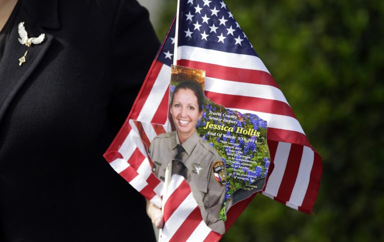 A guest leaving funeral services carries a U.S. flag and photo of Senior Deputy Sheriff Jessica Hollis, Wednesday, Sept. 24, 2014, in Austin, Texas. Hollis was swept away in a low water crossing during a period of heavy rainfall and flooding on Sept. 18. (AP Photo/Eric Gay)