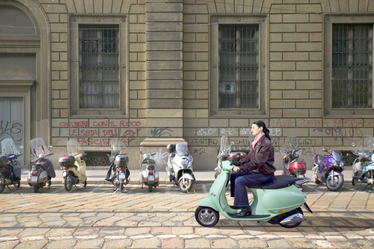 Side view of a woman riding a scooter on a street in Milan, Italy.