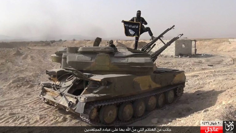 An Islamic State militant holds the group's flag as he stands on a tank they captured from Syrian government forces. (Rased News Network via AP, File)