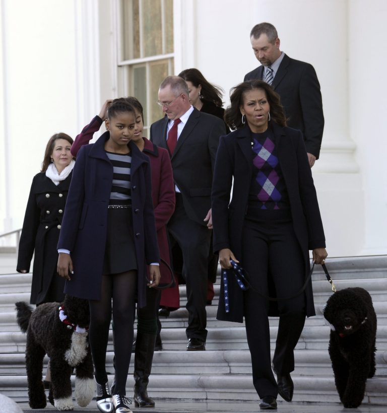 First lady Michelle Obama, right, with daughters Sasha, second from left, and Malia, partially hidden, walk outside to receive the Official White House Christmas Tree at the White House? in Washington, Friday, Nov. 29, 2013. (AP Photo/Susan Walsh)