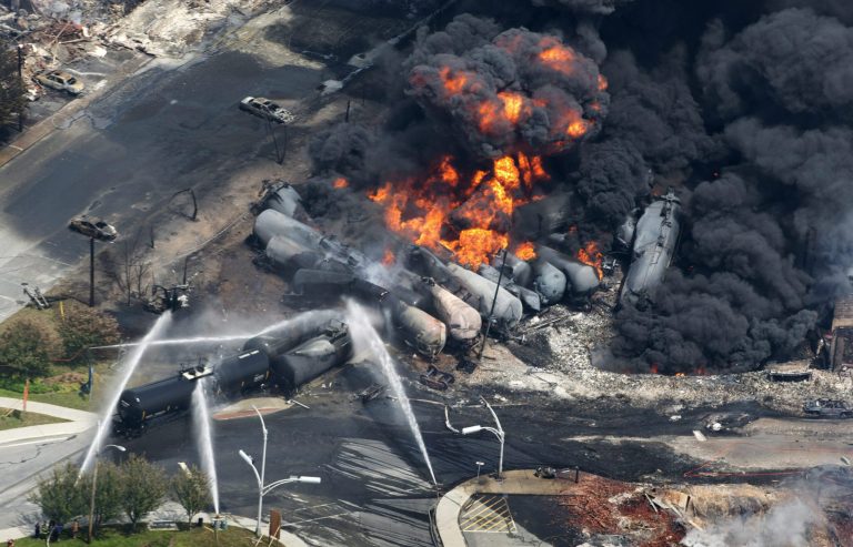 FILE - In this July 6, 2013 file photo, smoke rises from railway cars carrying crude oil after derailing in downtown Lac Megantic, Quebec. American Petroleum Institute President Jack Gerard said Tuesday that the oil and railroad industries are urging federal regulators to allow them as long as seven years to retrofit existing tank cars that transport highly volatile crude oil. (AP Photo/The Canadian Press, Paul Chiasson, File)