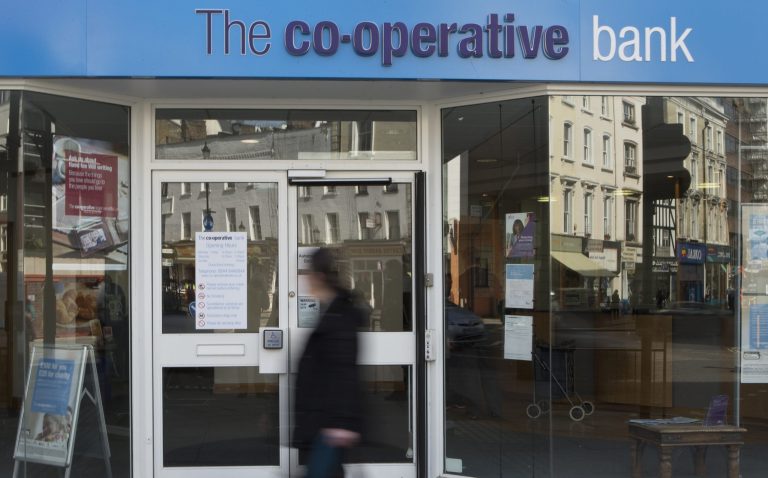 Pedestrians walk past a branch of the Co-operative Bank in central London, Thursday, April, 10, 2014. The Co-op group is Britain's largest mutual society, active in everything from food, funerals and its own bank. The group developed a 1.5 billion-pound ($2.4 billion) financial black hole, and agreed last year to a contentious rescue plan giving hedge funds a huge share of its operations. (AP Photo/Alastair Grant)