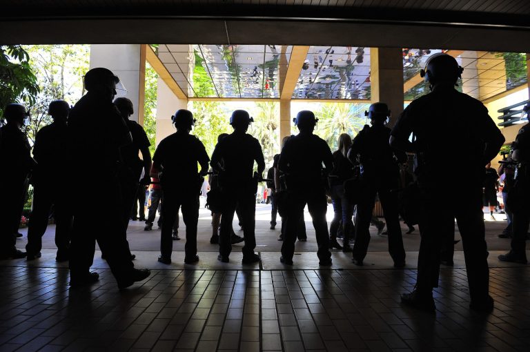 FILE - This July 24, 2012 file photo shows police at the entrance to city hall in Anaheim, Calif.  as demonstrators gathered on the steps to protest the death of Manuel Diaz, 25, who died as a result of gunshot wounds sustained during a police pursuit on Saturday. The killing of an unarmed black man by an officer in a nearly all-white police department in suburban St. Louis refocused the country on the racial balance between police forces and the communities they protect. But an analysis by The Associated Press found that the racial gap between black police and the communities where they work has narrowed over the last generation, particularly in departments that were once the least diverse. A much larger disparity now divides the low number of Hispanic officers in police departments. In Waco, Texas, for example, the community is more than 30 percent Hispanic, but the police department of 231 fulltime sworn officers has only 27 Hispanics. (AP Photo/The Orange County Register, Stuart Palley, File)   MAGS OUT; LOS ANGELES TIMES OUT
