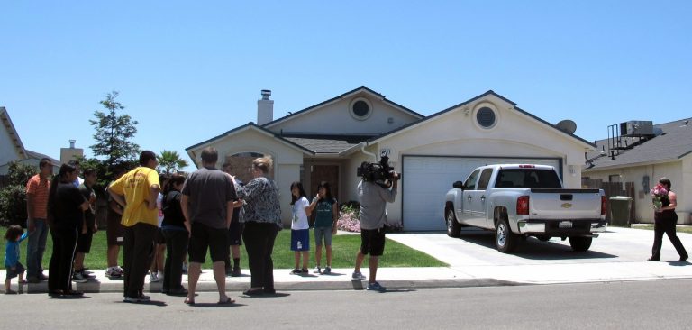   In this Sunday, June 10, 2012 photo, an unidentified woman, right, delivers flowers while classmates and neighbors gather in front of the Selma, Calif., house where Avtar Singh, a former Indian Army officer wanted in a 1996 killing in the disputed Kashmir region, killed his wife and two of their children in their California home. Selma police found Singh, 47, dead in his living room. His 36-year-old wife and three-year-old son were dead in a bed in the master bedroom. His 17-year-old son lay dead in his bedroom. A third son, 15 years old, was barely alive in another room and later died. All had been shot in the head. (AP Photo/Gosia Wozniacka)  