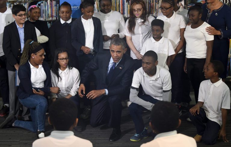 President Barack Obama gets down on his knee to pose with a group of students at Anacostia Library in Washington, Thursday, April 30, 2015, following a live 