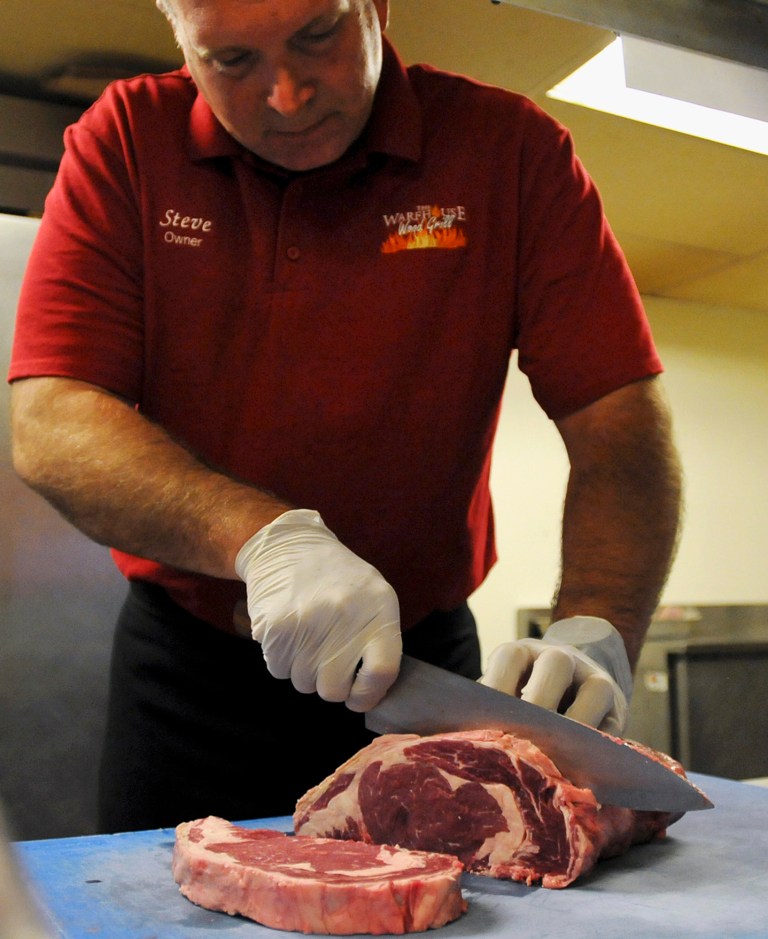 In this July 16, 2014 photo, Steve Long, owner of the Warehouse Wood Grill in Bourbonnais, Ill., cuts steaks in preparation for the weekend. Restaurants and other businesses in Bourbonnais are getting ready for arrival of football fans when the Chicago Bears begin their training camp July 25 at Olivet Nazarene University. (AP Photo/ The Daily Journal, Tiffany Blanchette)