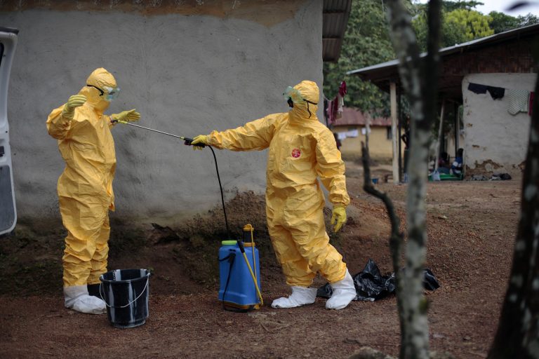 FILE - In this Tuesday, Sept. 30, 2014, file photo, Gordon Kamara, left, is sprayed by Konah Deno after they loaded six patients suspected to have been infected by the Ebola virus into their ambulance in the village of Freeman Reserve, about 30 miles north of Monrovia, Liberia. Ebola has killed more than 4,500 people in West Africa and wreaked havoc on the region, but some Africans see a bright side: The virus has been limited to five countries. It has even been beaten back in two of those countries. (AP Photo/Jerome Delay, File)