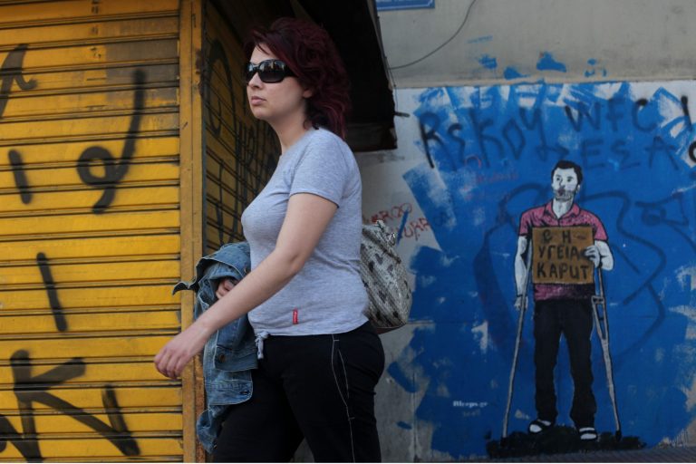  A woman walks past a mural of a figure in crutches and holding a sign that says 