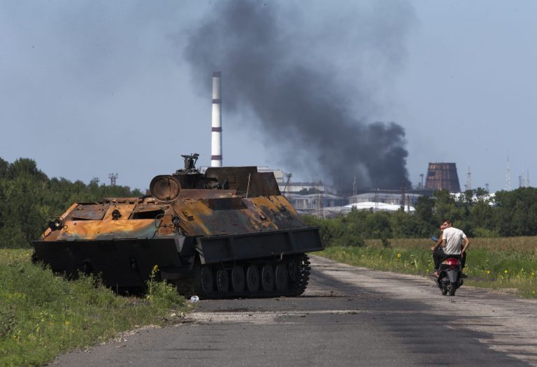 People ride a scooter past a destroyed pro-Russian fighters' APC near the city of Lisichansk, Luhansk region, eastern Ukraine Saturday, July 26, 2014. Volunteers from the Donbas Battalion, a volunteer militia for a united Ukraine, told The Associated Press their units, along with the Ukrainian army, regained control of Lisichansk on Friday. (AP Photo/Dmitry Lovetsky)