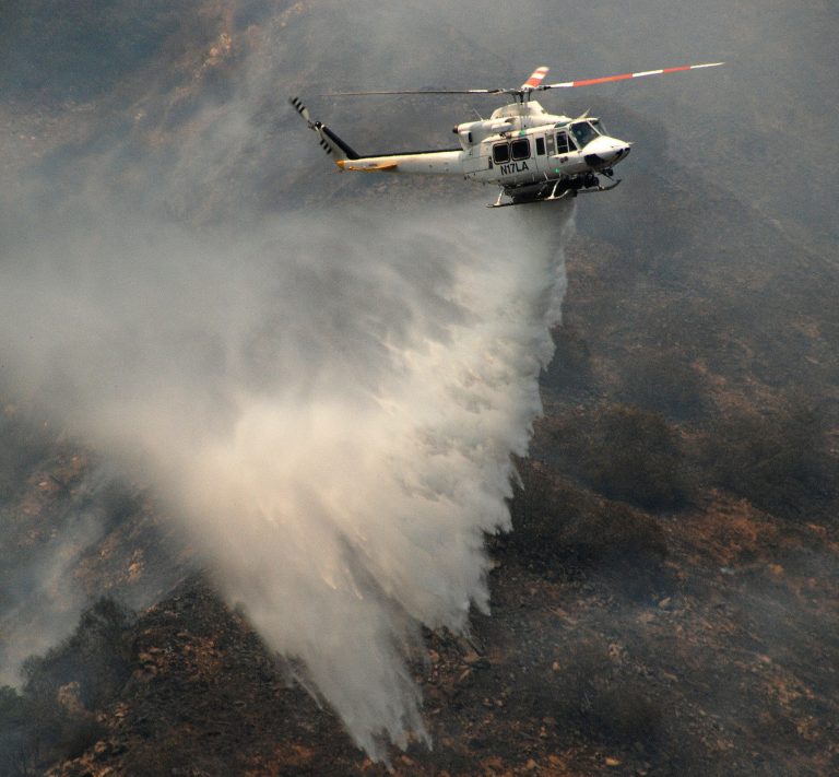 A firefighting helicopter makes a water drop on a brushfire  in Glendale,  Calif., Sunday June 22, 2014.   Firefighters from several agencies are battling the blaze from the ground and the air. (AP Photo/Mike Meadows)