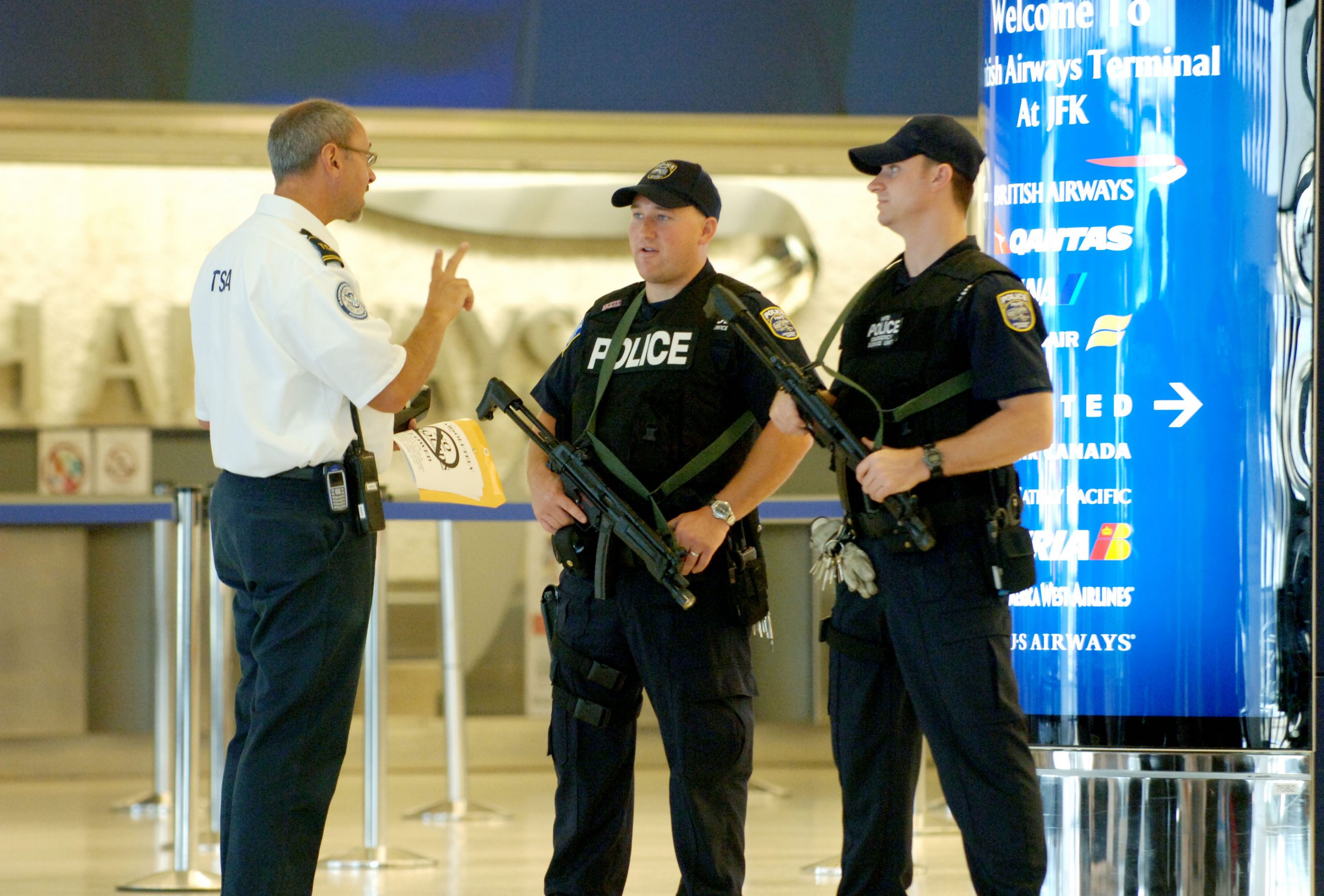 Passengers walk through JFK airport security, metal detectors buzzing