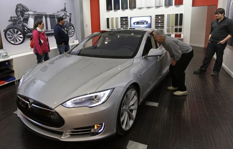 FILE - In this March 17, 2014 file photo, Tesla representative John Van Cleave, right, shows customers Sarah and Robert Reynolds, left, and Vince Giardina, a new Tesla all electric car, at a Tesla showroom inside the Kenwood Towne Centre in Cincinnati. Tesla reports quarterly earnings on Wednesday, May 7, 2014. (AP Photo/Al Behrman, File)