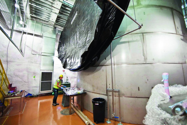 In this July 31, 2012 photo provided by Sanford Lab, Mikayla Thompson, of Yale University, works near the exterior of the water tank for the Large Underground Xenon experiment a mile beneath the earth's surface in a shuttered gold mine in Lead, S.D. The experiment, known as LUX, could begin collecting data as early as February _ and, if all goes as planned, that data could answer age-old questions about the universe and its origins, scientists said Monday, Nov. 19, 2012. (AP Photo/Courtesy of Sanford Lab, Matt Kapust)
