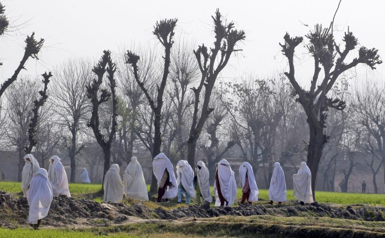 Women walk near the site of an attack on the outskirts of Peshawar, Pakistan, Wednesday, Feb. 12, 2014. Militants killed several members of an anti-Taliban militia on Wednesday in Pakistan's northwestern city of Peshawar, police said. (AP Photo/Mohammad Sajjad)