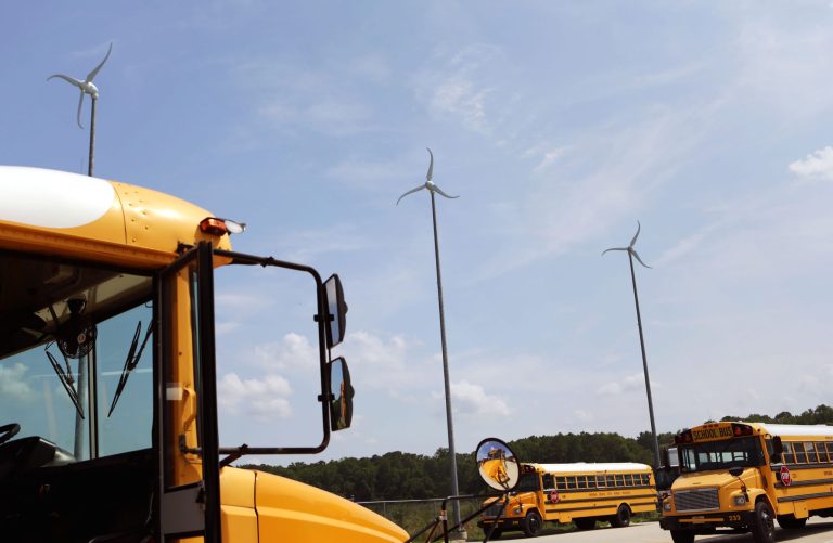 ADVANCE FOR SATURDAY, JULY 12 - Wind turbines turn in the breeze on Wednesday, July 2, 2014, at a Virginia Beach Public School bus yard in Virginia Beach, Va. Budgets are tight, so school divisions around the nation are looking for ways to cut costs. In 2005, the U.S. Energy Department launched the Wind for Schools project to help those interested in tapping into that power source. By last year, more than 130 systems had been installed at schools in 11 states, including more than a dozen across Virginia and North Carolina. (AP Photo/The Virginian-Pilot, Vicki Cronis-Nohe)