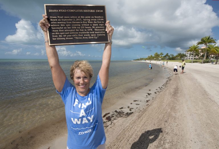 In this photo provided by the Florida Keys News Bureau, Diana Nyad poses with a bronze plaque Monday, Sept. 1, 2014, at Smathers Beach in Key West, Fla. The plaque commemorates Nyad's 2013 Cuba-to-Florida Keys swim. She arrived at Smathers Beach the early afternoon of Sept. 2, 2013, to become the first person to ever swim  from Havana to Key West without a shark cage. (AP Photo/Florida Keys News Bureau, Andy Newman)