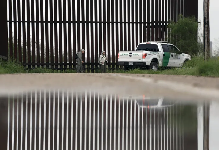 In this Sunday, Nov. 13, 2016, photo, a U.S. Customs and Border Patrol agent passes birdwatchers Rayborn and Nancy Hill along a section of border wall in Hidalgo, Texas. The idea of a concrete wall spanning the entire 1,954-mile southwest frontier collides head-on with multiple realities, like a looping Rio Grande, fierce local resistance, and cost. (AP Photo/Eric Gay)