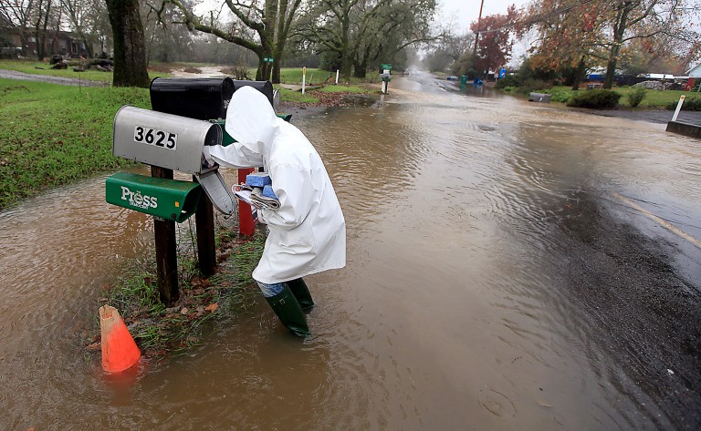   Sandy LeDuc braves floodwaters to gather her mail on Piner Road, Friday Dec. 21, 2012 in Santa Rosa, Calif as a large winter storm barreled in to Northern California. (AP Photo/The Press Democrat, Kent Porter)  