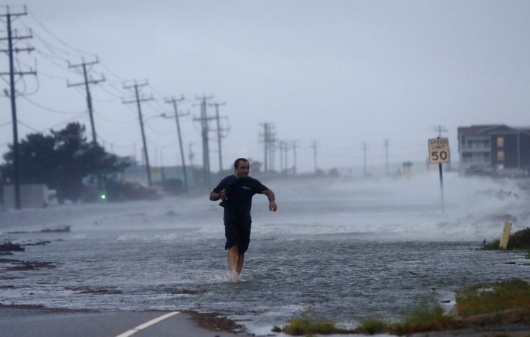 FILE - In this July 4, 2014 file photo, a man crosses a flooded Highway 64 as wind pushes water over the road as Hurricane Arthur passes through Nags Head, N.C. This year's Atlantic hurricane season has so far had the fewest number of storms since 1983, with only five named storms forming so far in the region: Arthur, Bertha, Cristobal, Dolly and Edouard. (AP Photo/Gerry Broome, File)