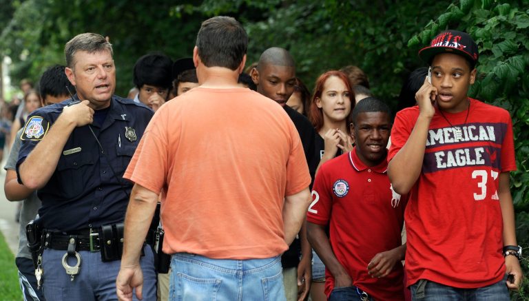 A Baltimore County police officer speaks to a parent as students are evacuated from Perry Hall High School after a student was shot and critically wounded on the first day of classes Monday, Aug. 27, 2012, in Perry Hall, Md. A suspect was taken into custody shortly after the shooting, according to police. No one else was reported injured. (AP Photo/Steve Ruark)