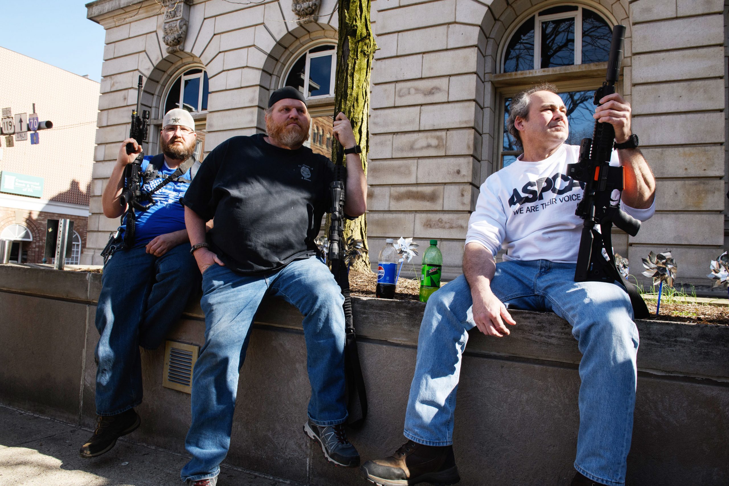 Men sit along a wall holding their AR-15 style rifles at a rally to support Martin Palla and gun rights on April 22 in the courtyard of the Westmoreland County Courthouse in Greensburg, Pa.