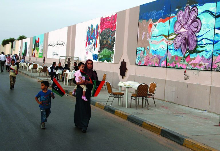 In this Tuesday, Oct. 23, 2012 photo, a Libyan family in Tripoli walk by a mural exhibition celebrating one year since the fall of dictator Muammar Gadhafi in Tripoli, Libya. One year on, the country is still trying to overcome the legacy of one of the most erratic leaders of modern times as well as a brutal eight month struggle that left the country awash in weapons, militias and very few viable institutions of the state. (AP/Paul Schemm)
