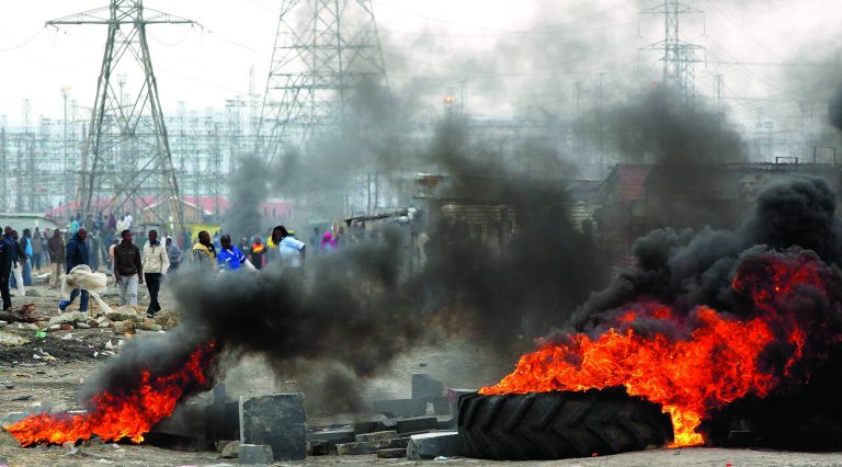 Miners burning tires as they barricade the streets in Lonmin Platinum Mine near Rustenburg, South Africa, Saturday, Sept. 8, 2012. As various stakeholders continued negotiations South African Justice Minister Jeff Radebe warned that the Government would clamp down on daily illegal marches by miners brandishing machetes, spears and clubs that have marked the strike. (AP Photo/Themba Hadebe)