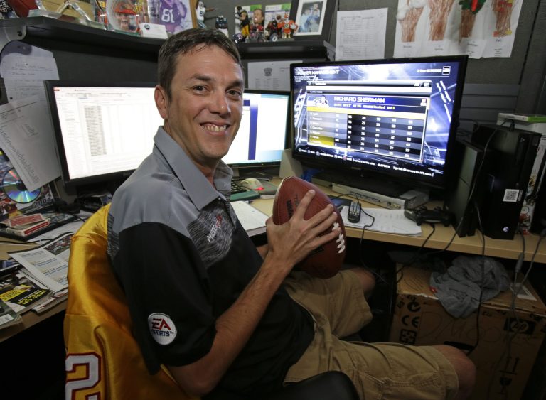 In this Wednesday, Aug. 6, 2014 photo, Donny Moore poses for a photo in front three computer screens he uses to rate NFL football players for the Madden NFL video football game at EA Sports in Orlando, Fla.  Moore is the 