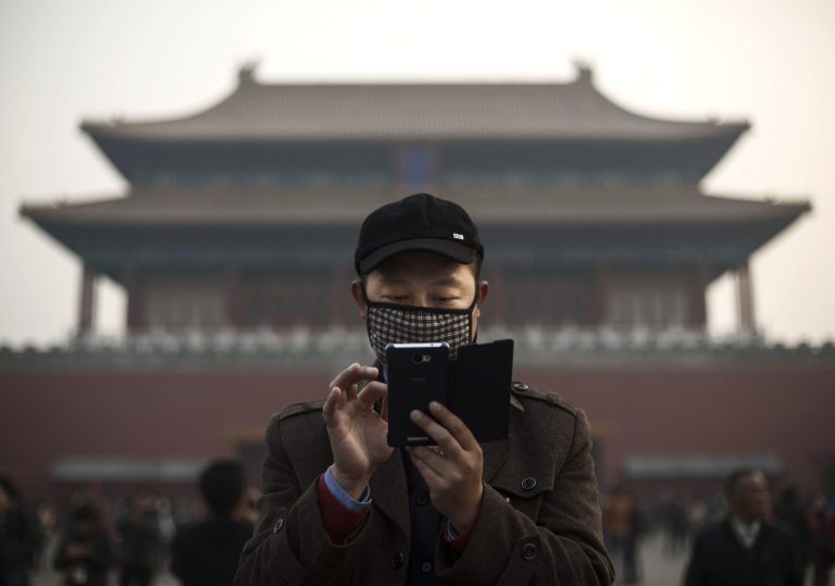 A Chinese man wears a mask to protect against pollution as he uses his smartphone on a hazy day outside the Forbidden City November 20, 2014 in Beijing, China. (Photo by Kevin Frayer/Getty Images)