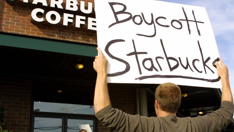 A protester holds a protest sign outside a Starbucks coffee shop.