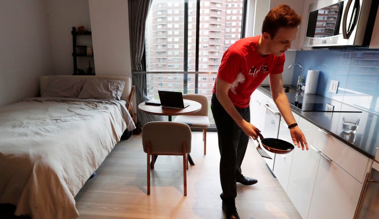 In this May 1, 2018, photo, Carmel Place resident Matthew Alexander puts away dishes in his studio apartment in the Kips Bay neighborhood of Manhattan borough in New York. After sharing space with roommates, Alexander moved into a co-living space building, where he likes the minimalist living style. Although the apartment is small, the building provides multiple amenities, including a once a week visit from a housekeeper, grocery delivery and dry cleaning pickup, plus a gym and a rooftop terrace.