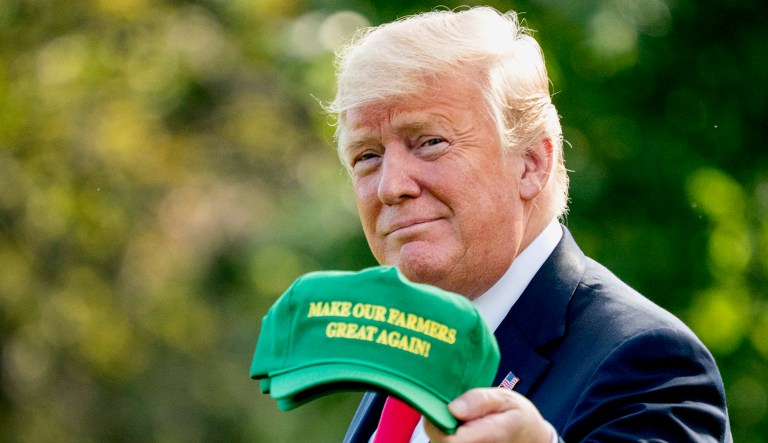 President Trump hold up hats that read "Make Our Farmers Great Again!" as he walks across the South Lawn before boarding Marine One at the White House in Washington, D.C.