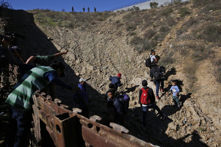 Migrants cross the U.S. border wall to San Diego, California from Tijuana, Mexico, Sunday, Dec. 16, 2018, before turning themselves in to U.S. border patrol agents, standing at the top.