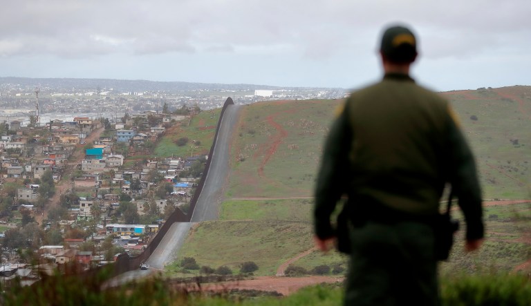 An officer on the American side of the U.S.-Mexico border walks near a wall.