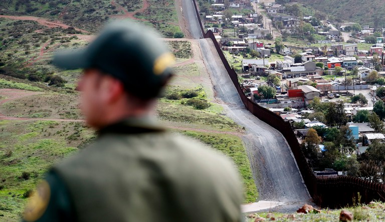 An officer on the American side of the U.S.-Mexico border walks near a wall.