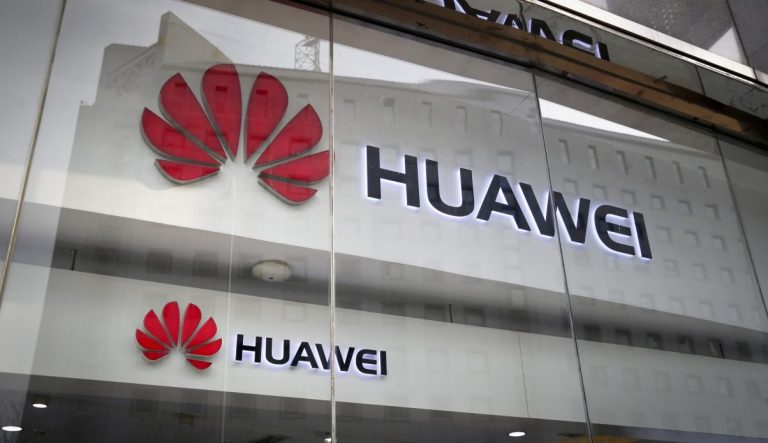 In this Jan. 29, 2019 photo, the logos of Huawei are displayed at its retail shop window reflecting the Ministry of Foreign Affairs office in Beijing.