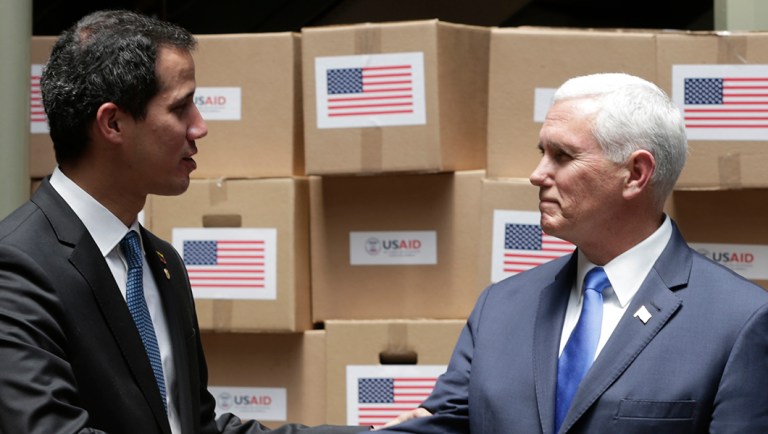 Venezuela's self-proclaimed interim president Juan Guaido, center, shakes hands with Vice President Mike Pence in a room filled with humanitarian aid destined for Venezuela.