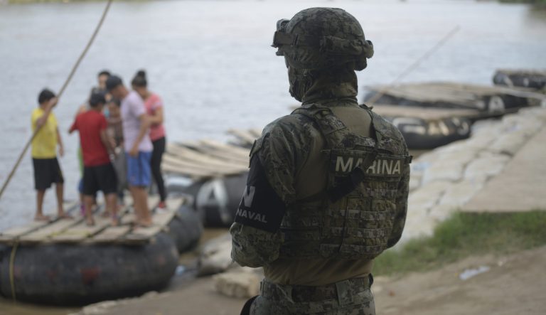 A Mexican marine stands guard on the Suchiate River, watching out for migrants crossing from Guatemala to Ciudad Hidalgo, as locals stand on a raft in Mexico, Sunday, June 16, 2019. Mexico faces heightened pressure from the U.S. to reduce the surge of mostly Central American migrants through its territory. 