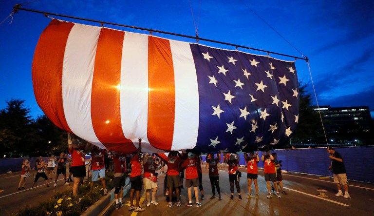 Volunteers raise the giant American flag that hangs over the starting line of a race.