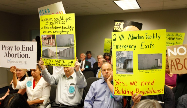 Protesters hold signs as they wait for the Virginia Board of Health meeting on abortion clinic regulations in Richmond, Va., Friday, Sept. 14, 2012.