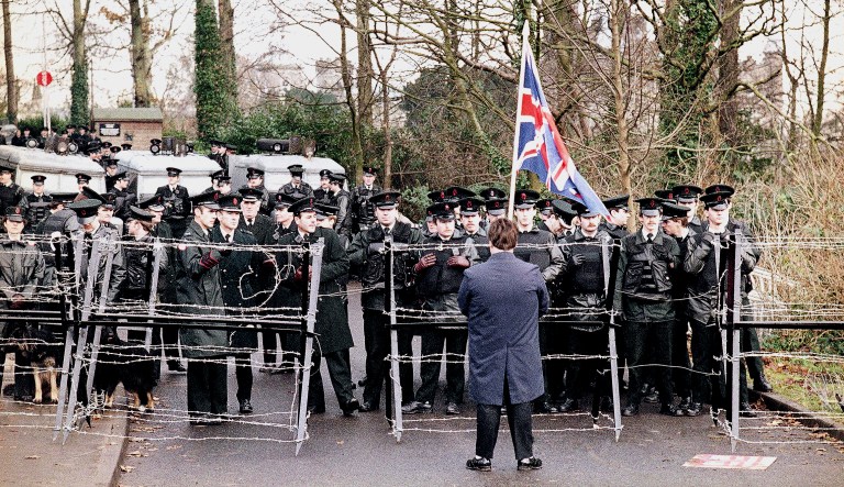 A lone Loyalist demonstrator, carrying the Union Jack, faces officers of the Royal Ulster Constabulary, as they seal off the road leading to Stormont, near Belfast, Northern Ireland, in December 1985.